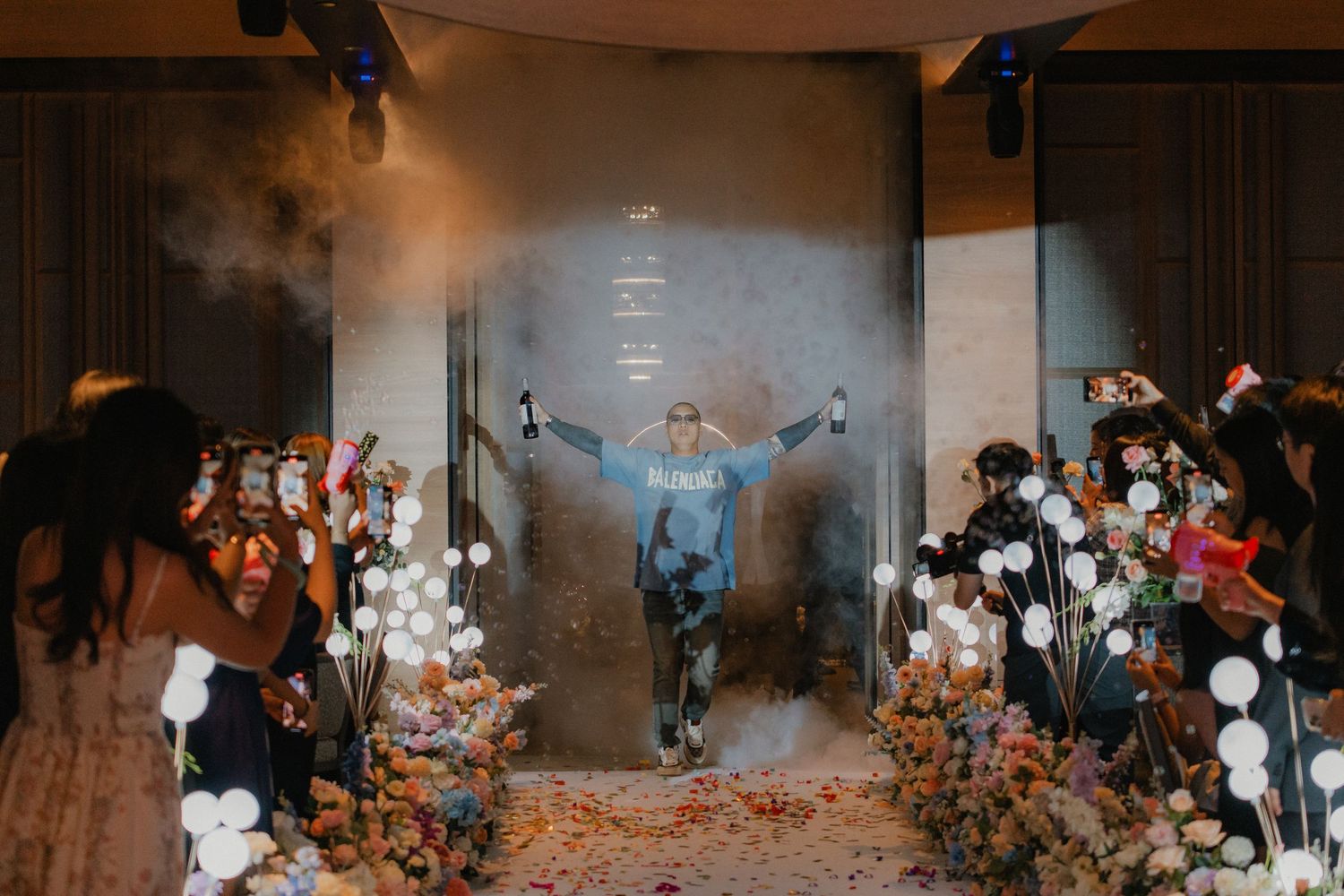 A celebration in a dimly lit venue with smoke effects and illuminated floral decorations along the aisle.