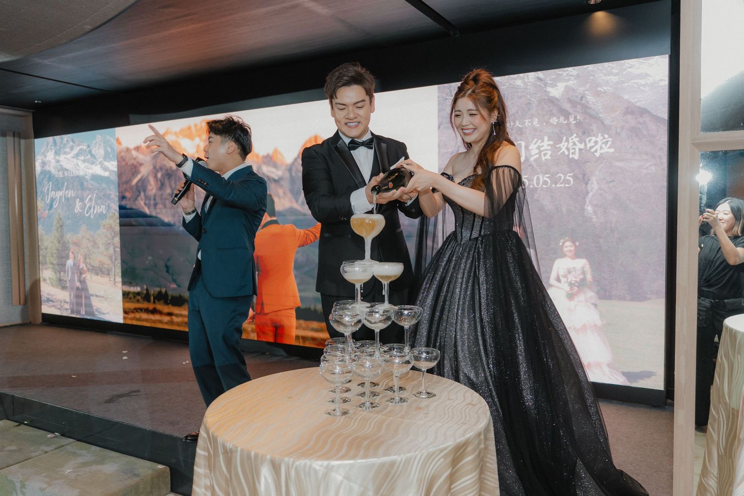 A champagne tower being poured at an elegant wedding reception with formal attire.