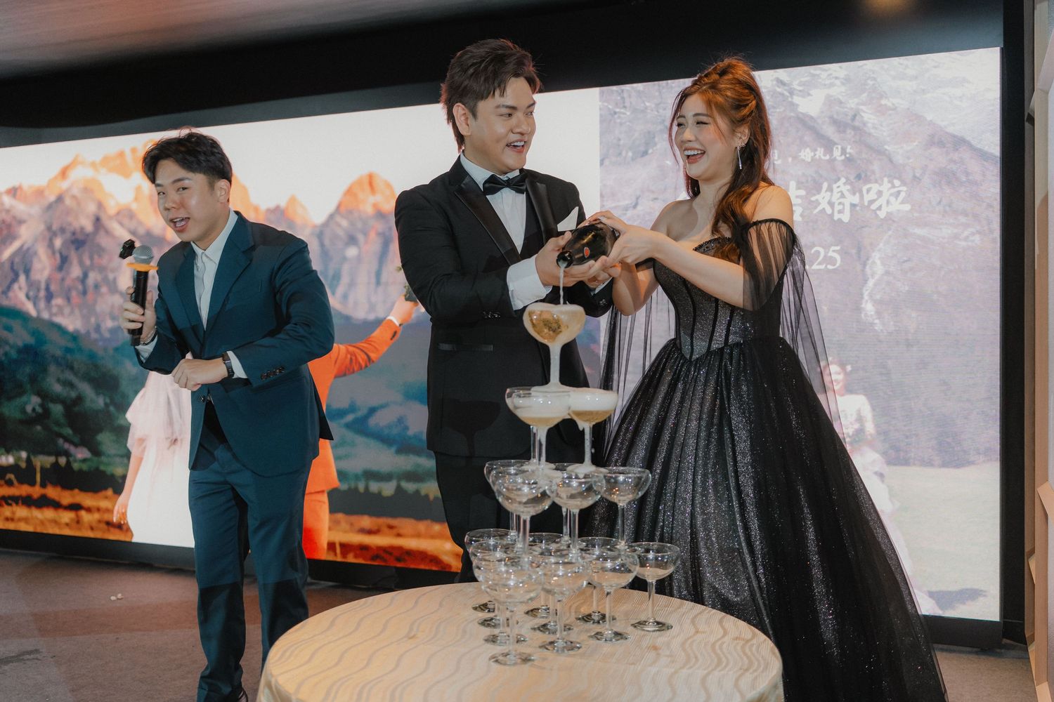 Guests pouring champagne into a tower of glasses at an elegant wedding reception.