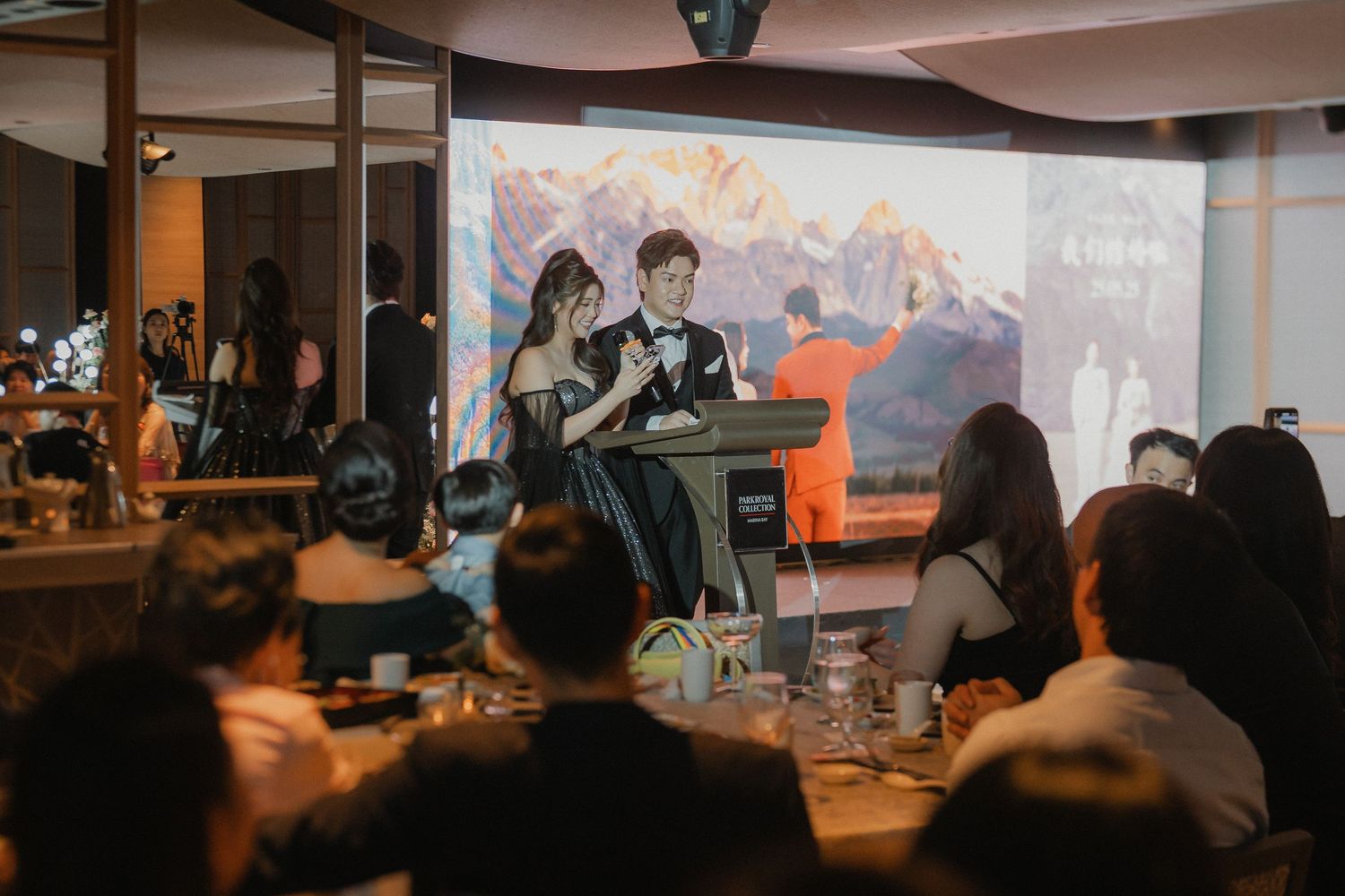 Performers entertain guests during evening wedding reception with mountain backdrop projection.