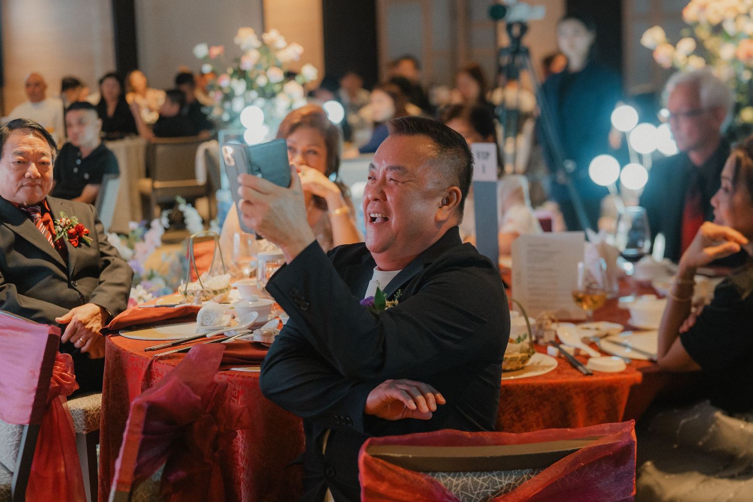 A guest laughs enthusiastically while sitting at a decorated banquet table during an indoor celebration event.