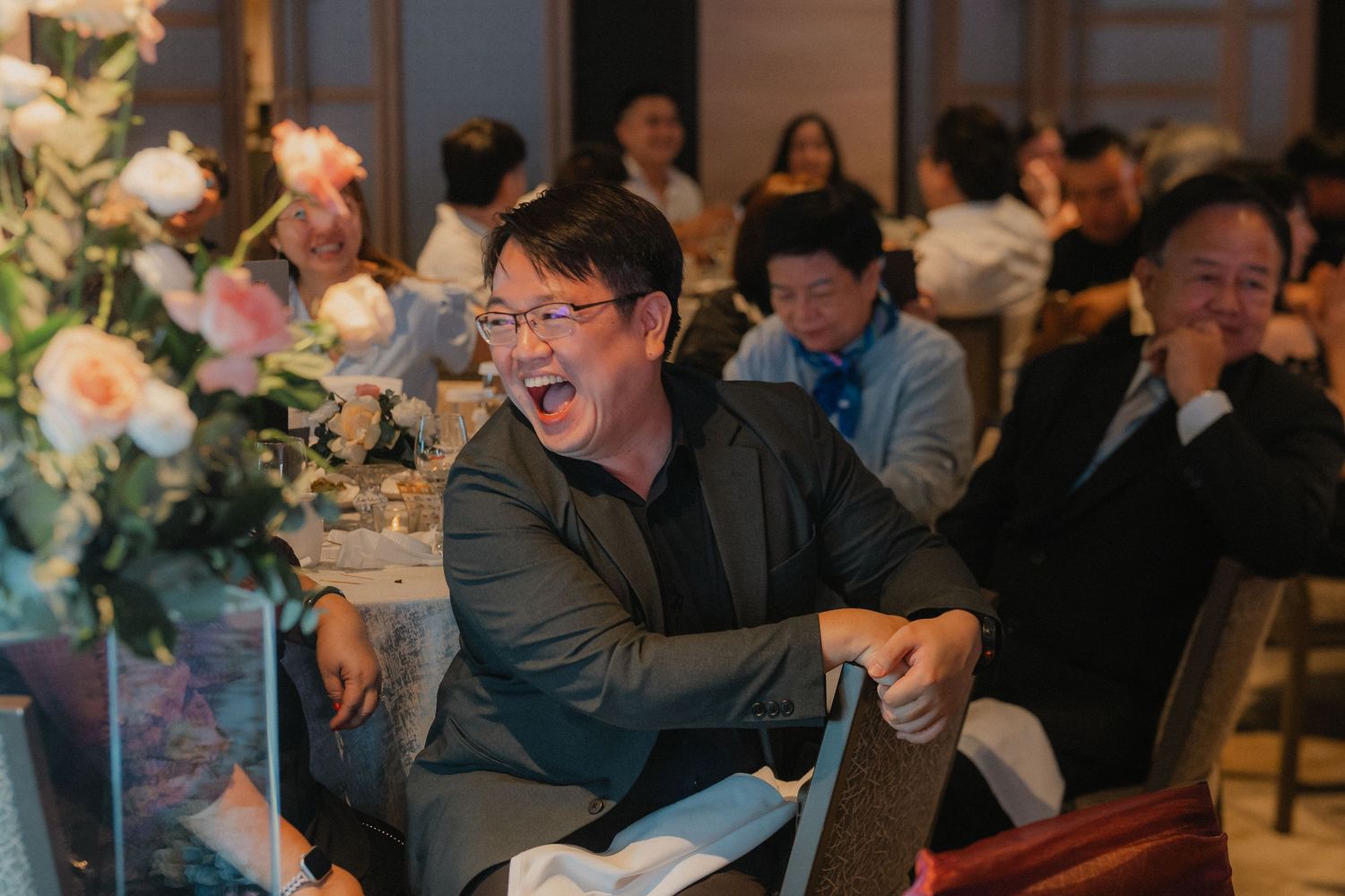 A crowd of guests celebrates at an indoor event with festive lighting and decorative elements in the background.