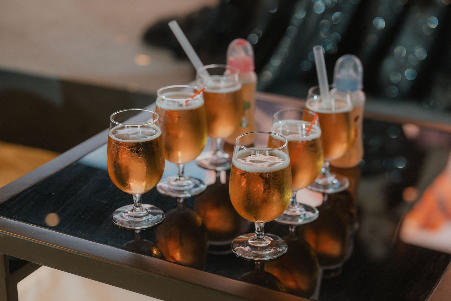 Several glasses of golden beer are lined up on a dark bar surface with ambient lighting.