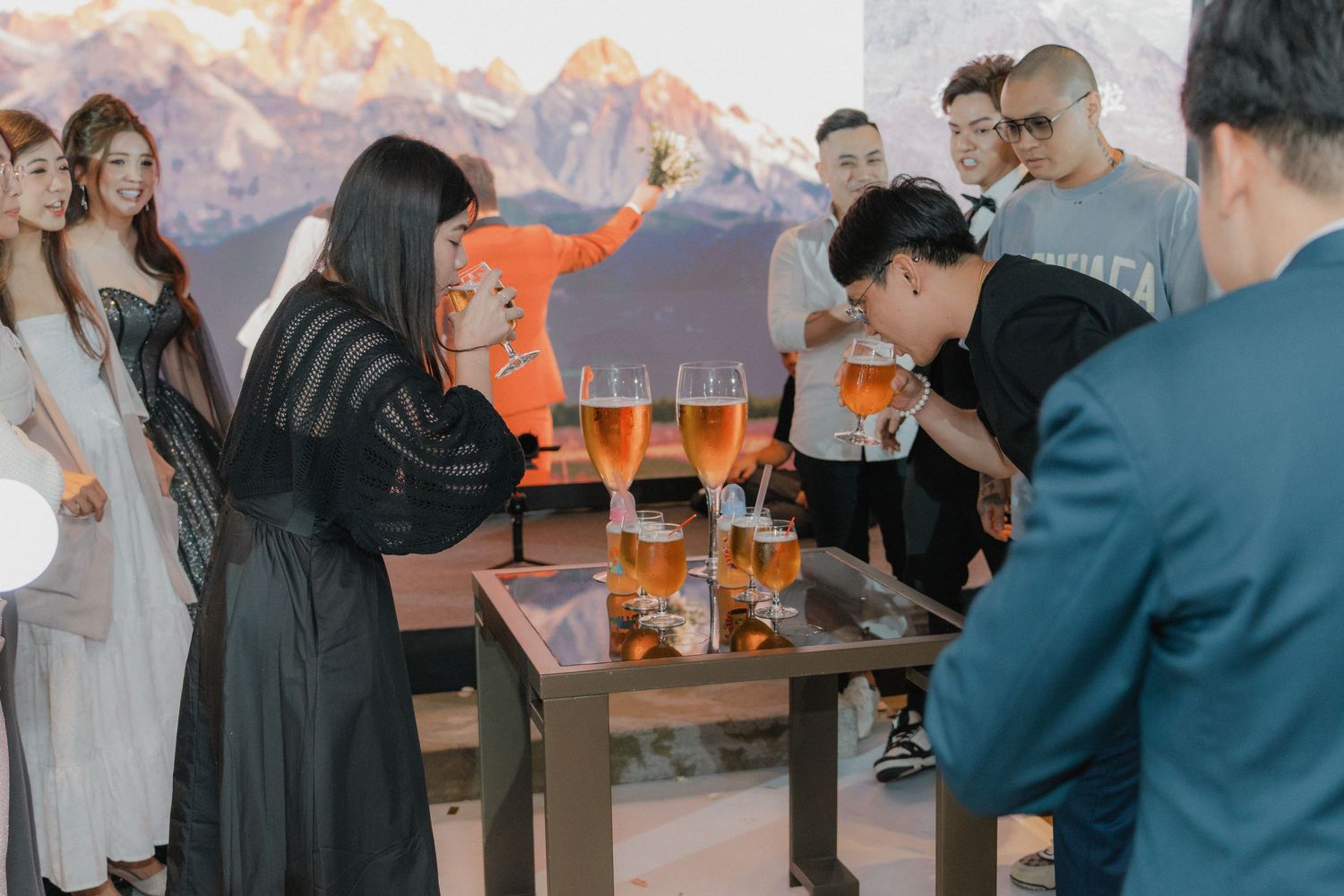 People gathered around tables celebrating with drinks and snacks against a mountain backdrop.