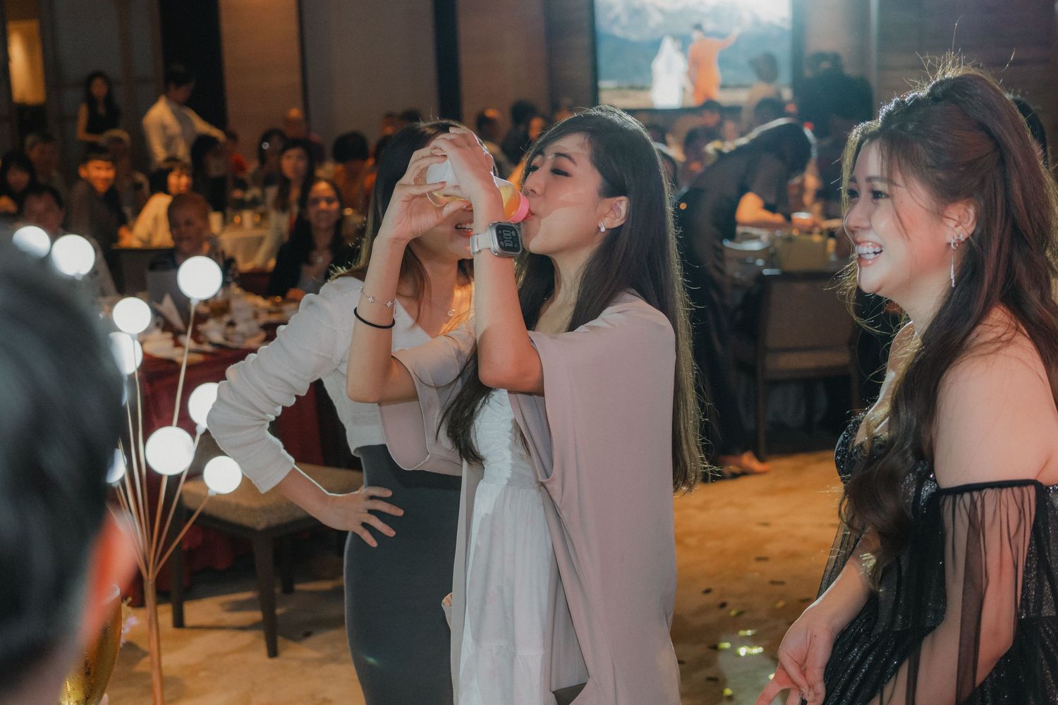 People enjoying a lively celebration in an indoor venue with decorative lights.