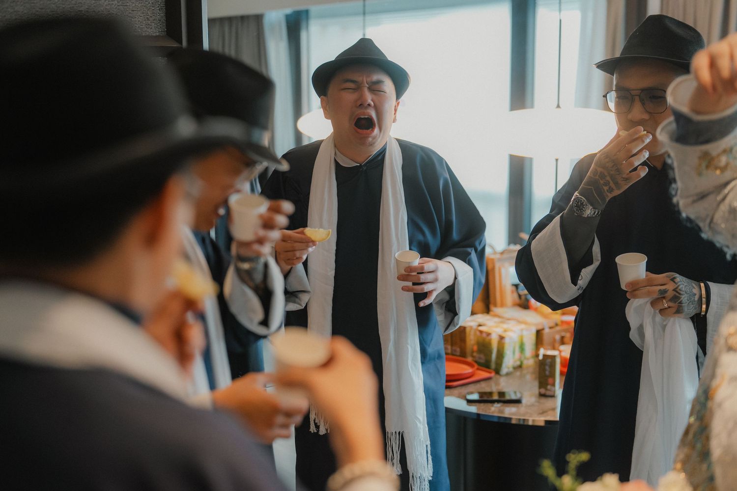 Guests in formal attire and hats socializing at an indoor celebration.