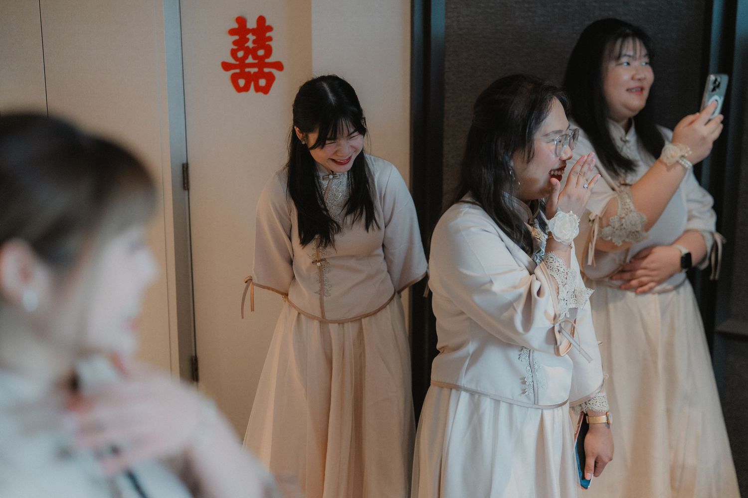 Bridesmaids in light-colored dresses react emotionally during a wedding celebration with a double happiness symbol.