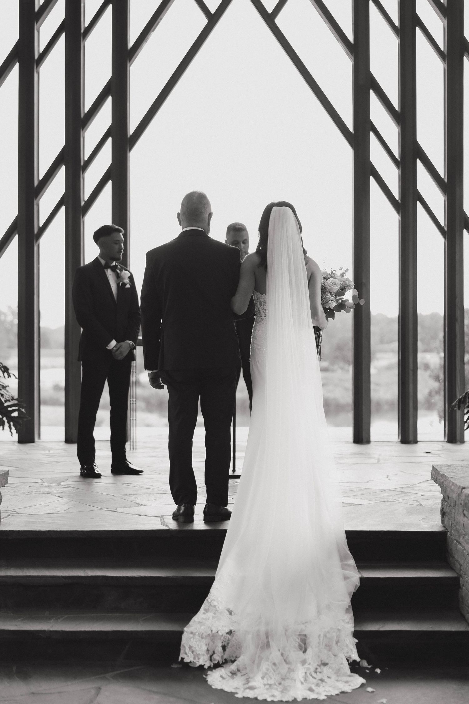 Black and white wedding reception photograph showing elegant silhouettes against tall vertical windows.