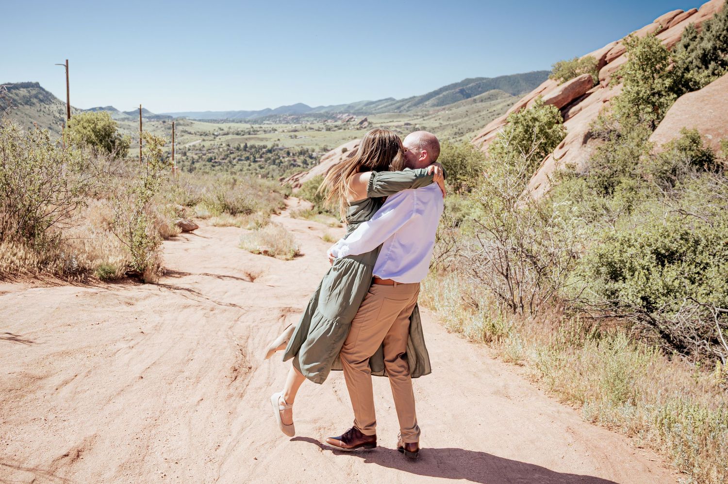 Couple embracing and dancing on a desert trail surrounded by mountains and desert vegetation.