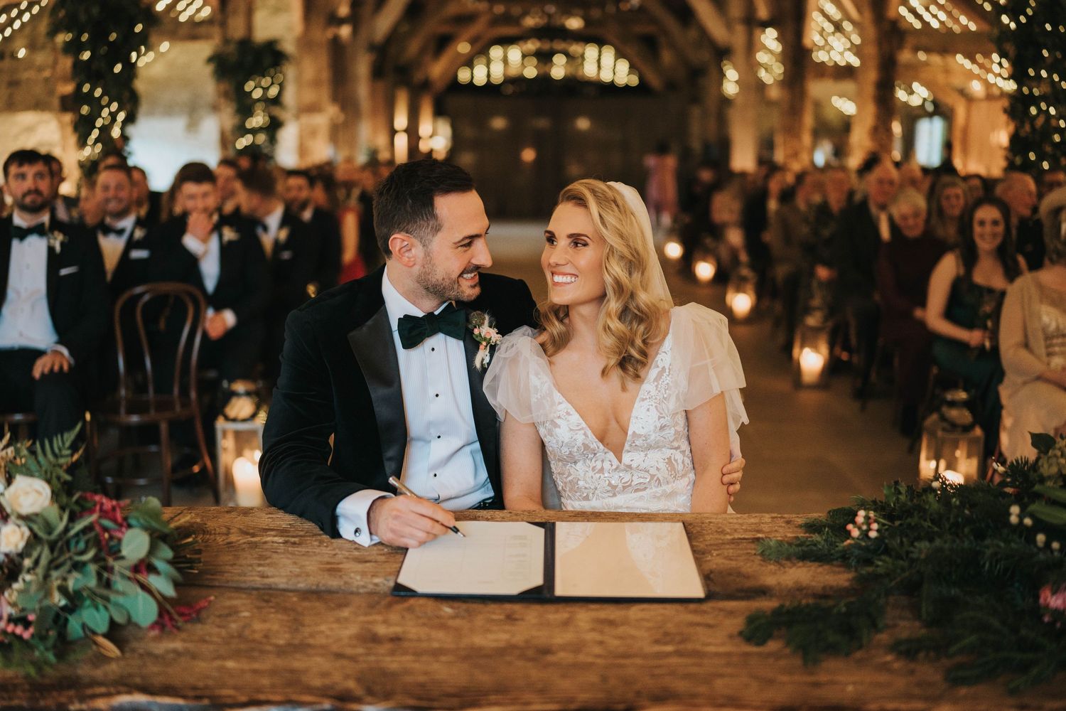A romantic wedding scene with rustic barn setting illuminated by warm candlelight and floral decor.