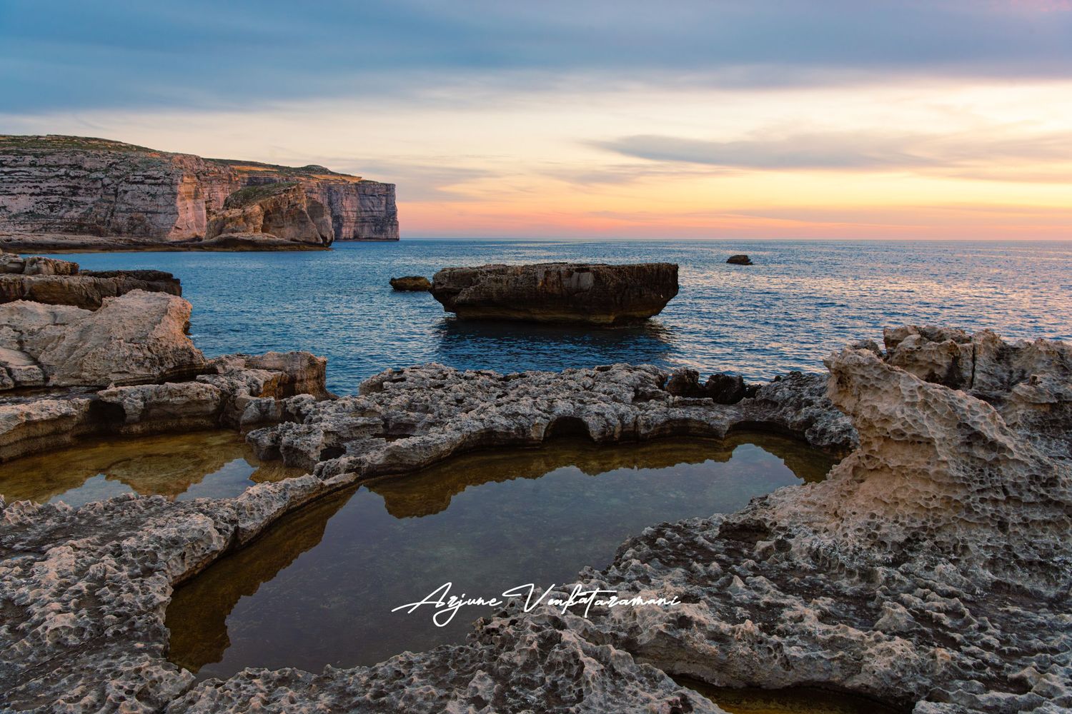 Rocky coastal pool at sunset with dramatic cliffs and calm sea in the background, Malta.