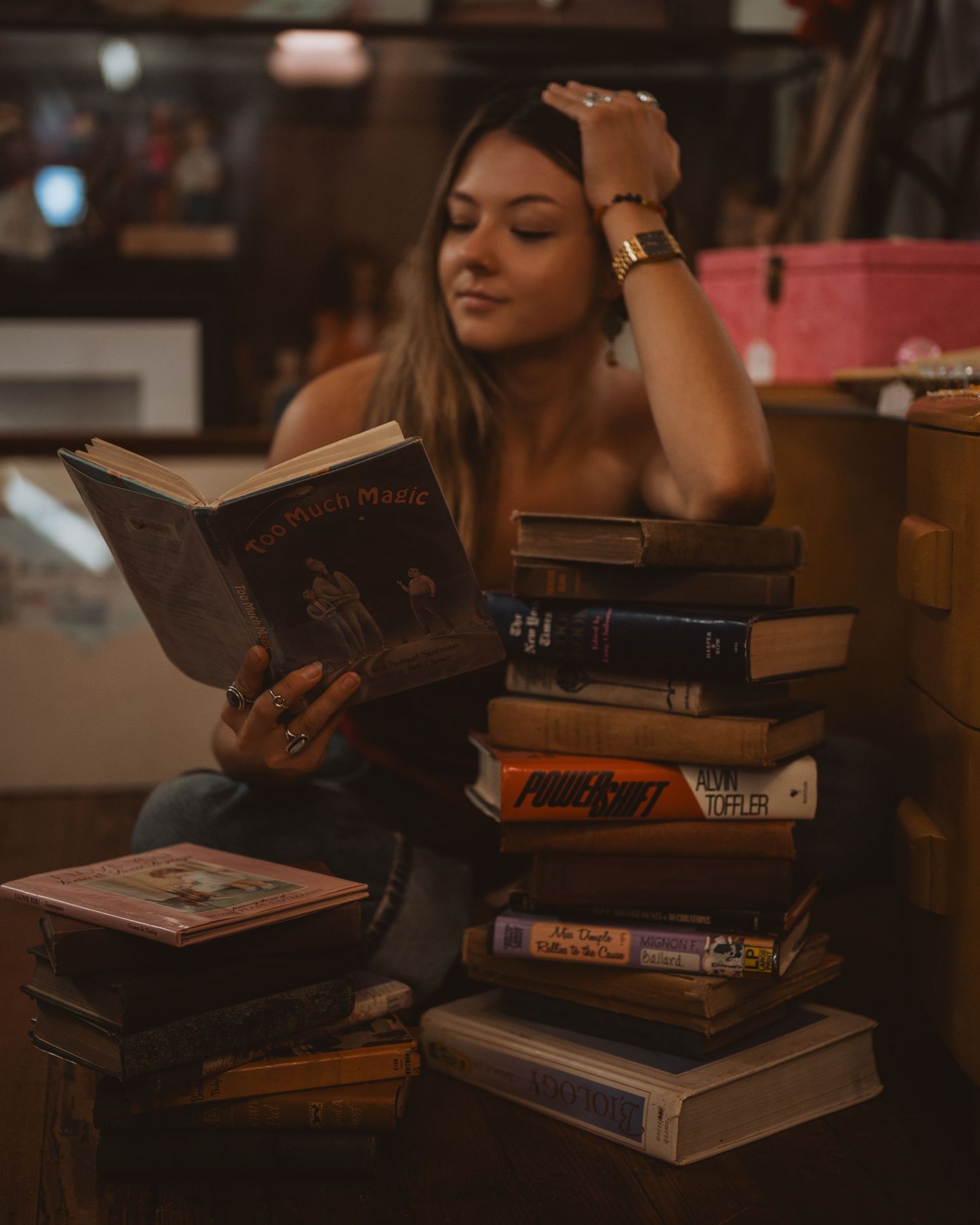 Student studies with a large stack of textbooks in warm lighting while sitting at wooden table.
