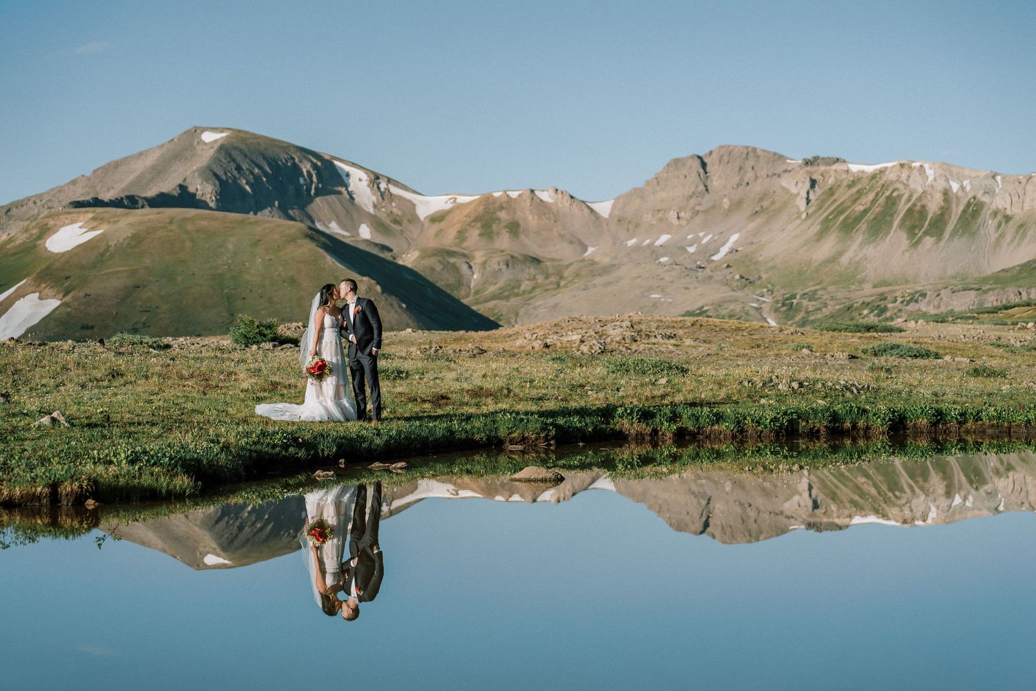 A couple embraces in a snowy winter landscape with majestic snow-capped mountains rising in the background. Aspen elopement photography.