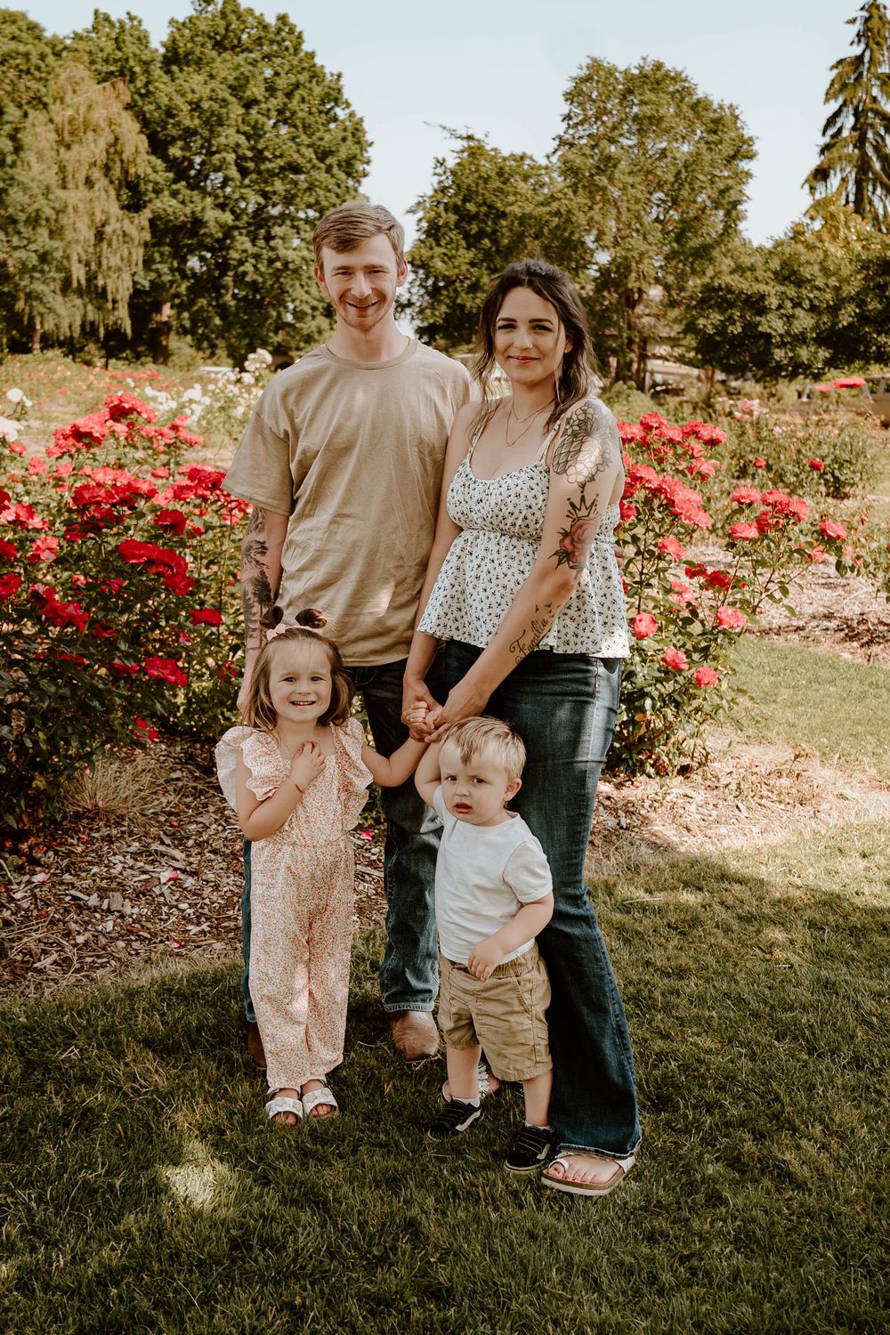 Happy young family of four poses together in a beautiful rose garden on a sunny day.