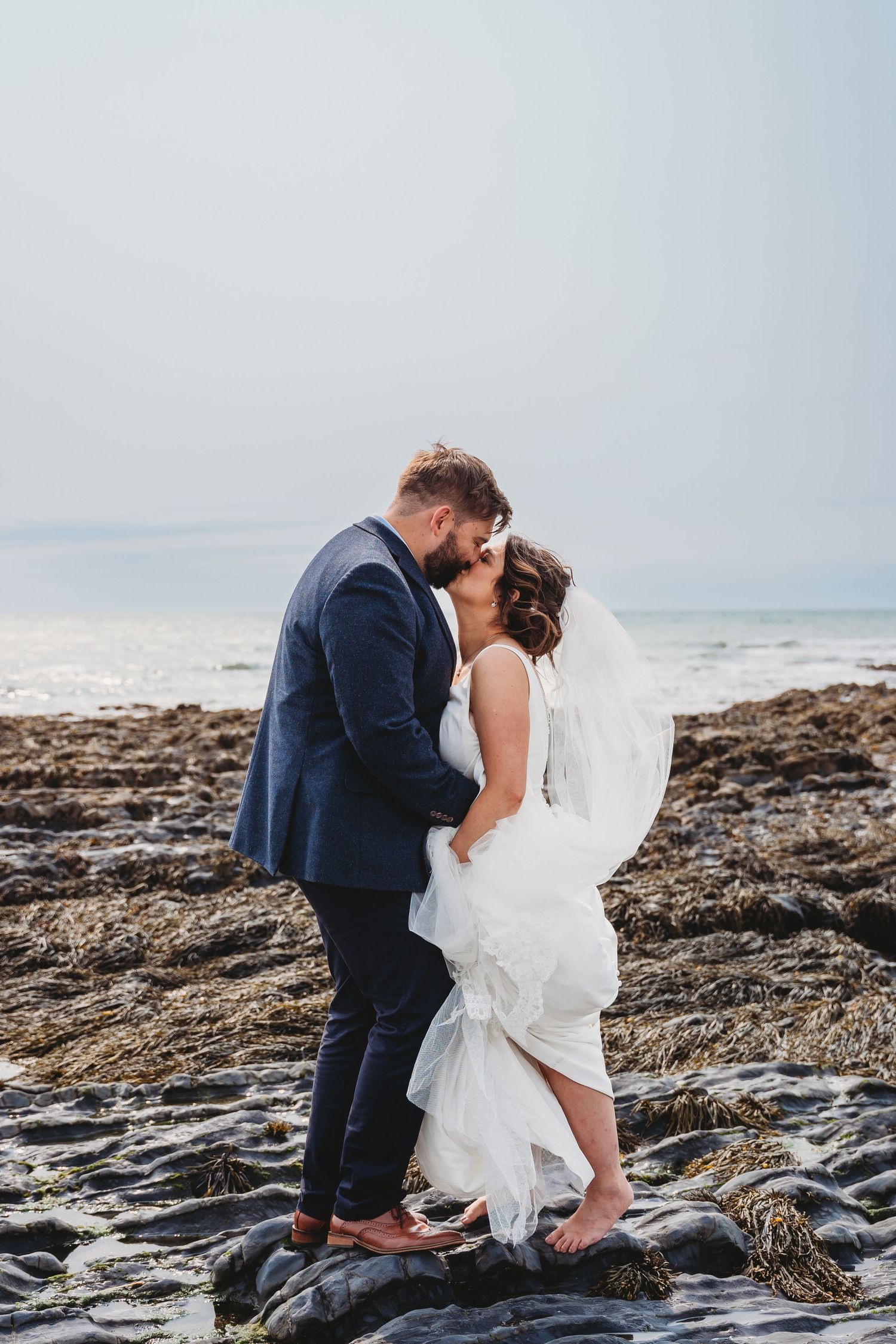 A romantic wedding pose on rocky coastal shores with ocean in background.