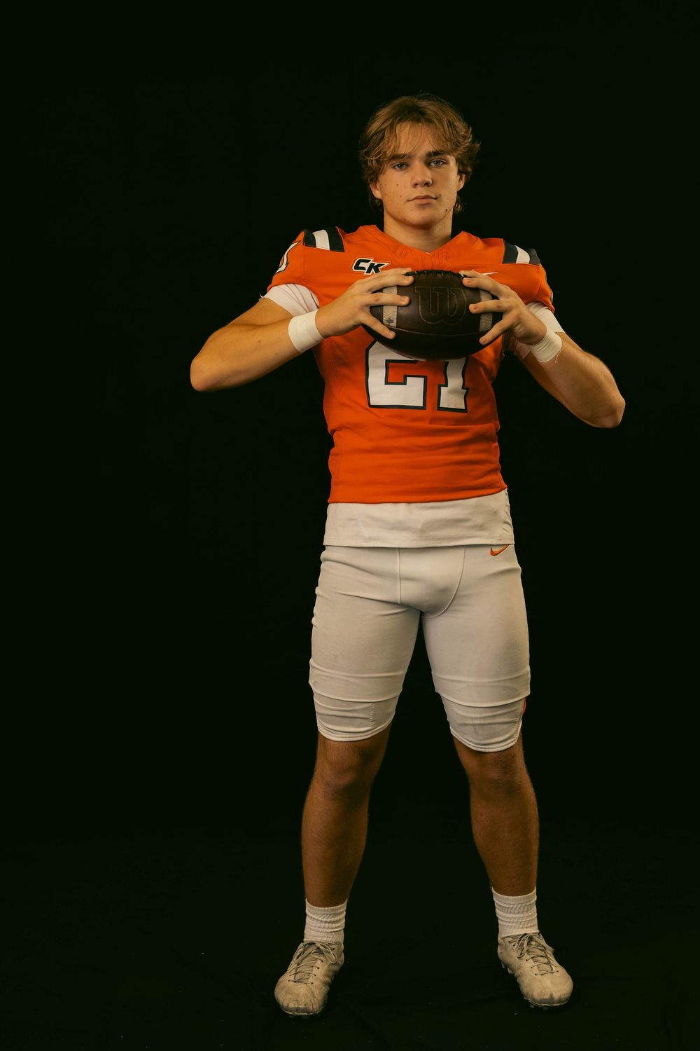 Football player in orange uniform makes dynamic poses with arms and legs in a studio setting.