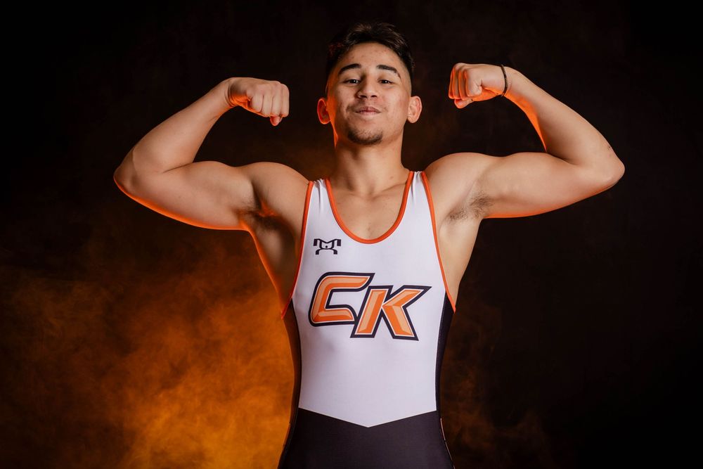 Athletic figure in sleeveless white wrestling singlet showing bicep flex poses against dark background.