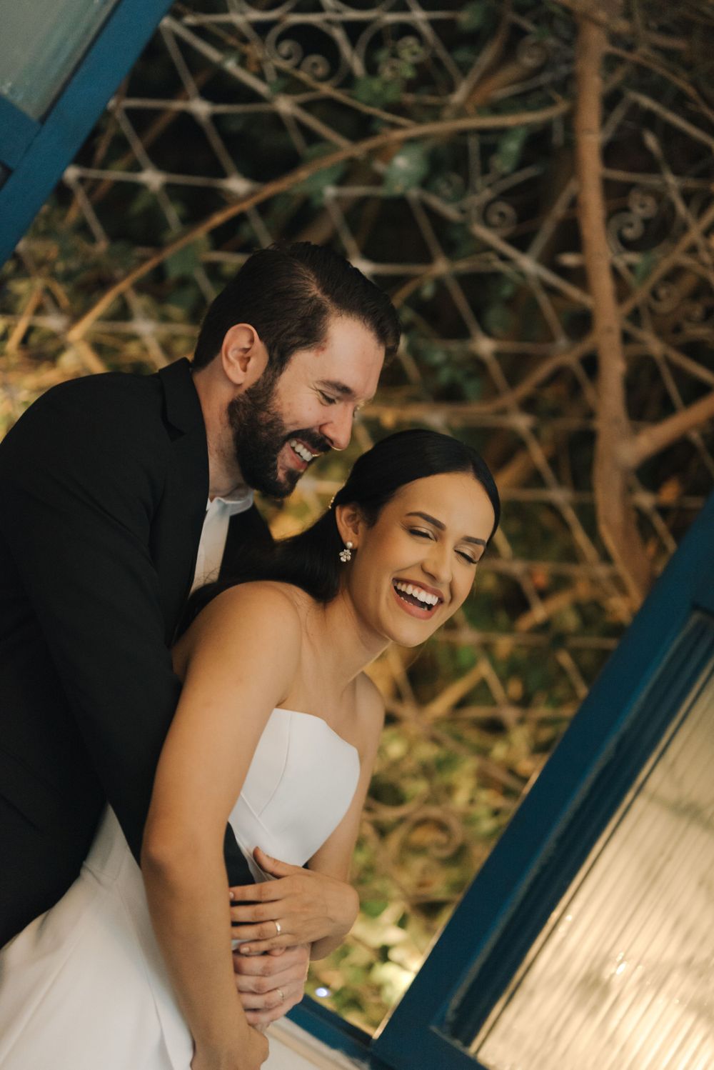 A happy couple sharing laughter together during an evening celebration beside decorative lighting.