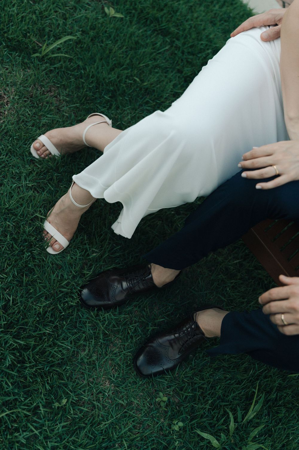 Close-up view of two people sitting on grass wearing contrasting black and white clothing and dress shoes.