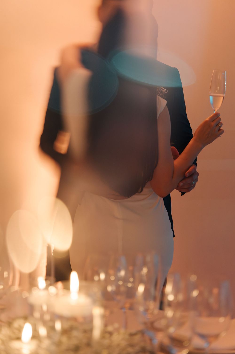 Blurred silhouettes of people holding drinks at an elegant candlelit dinner party with wine glasses on the table.