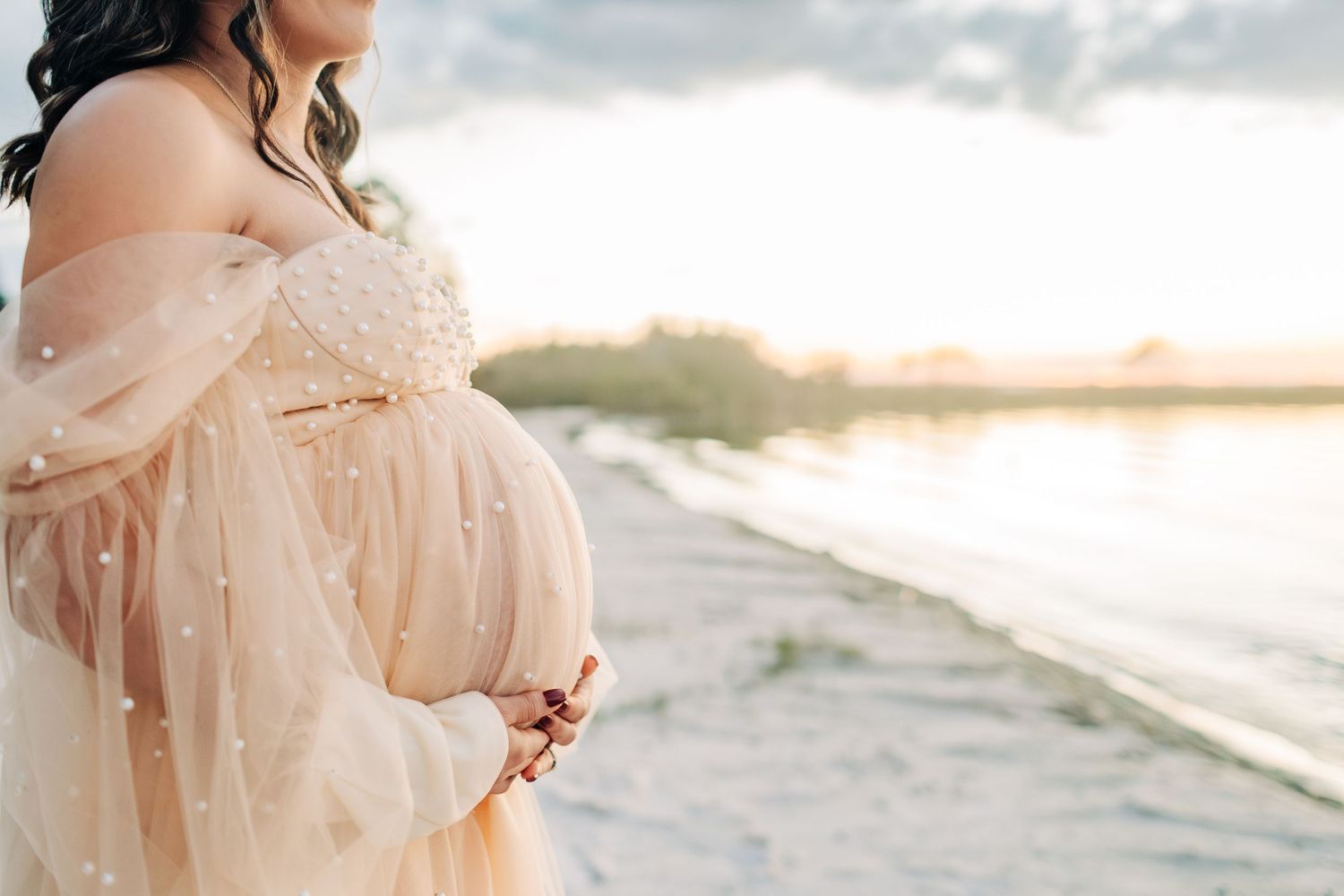 Beautiful close up of a pregnant mom holding her belly during a sunset beach photo session in Orlando