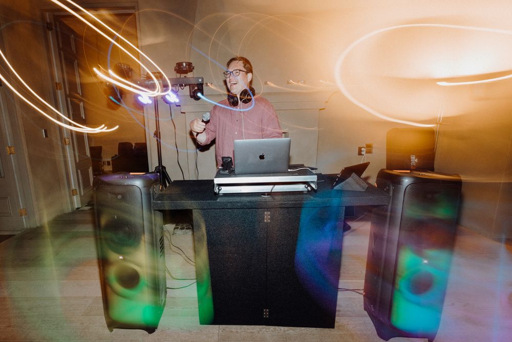 A DJ performs at a darkened venue with glowing green lights and smoke effects, captured by Apertured Media Auckland Wedding Photographer.