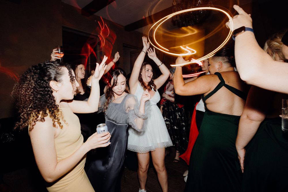 The bride and guests dance and celebrate on a dark dance floor, captured by Apertured Media Auckland Wedding Photographer.