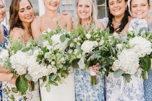Bridesmaids in blue floral dresses hold elegant white and green bouquets with hydrangeas and eucalyptus.