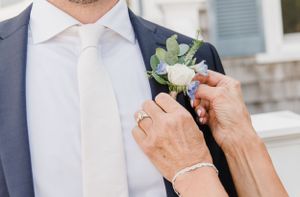 Hands pinning a delicate succulent and white flower boutonniere onto a navy blue suit lapel.