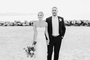 Black and white photo of a couple on their wedding day standing by a rocky beach coastline.