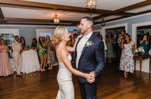 A couple shares their first dance together at their wedding reception on a wooden dance floor while guests watch.