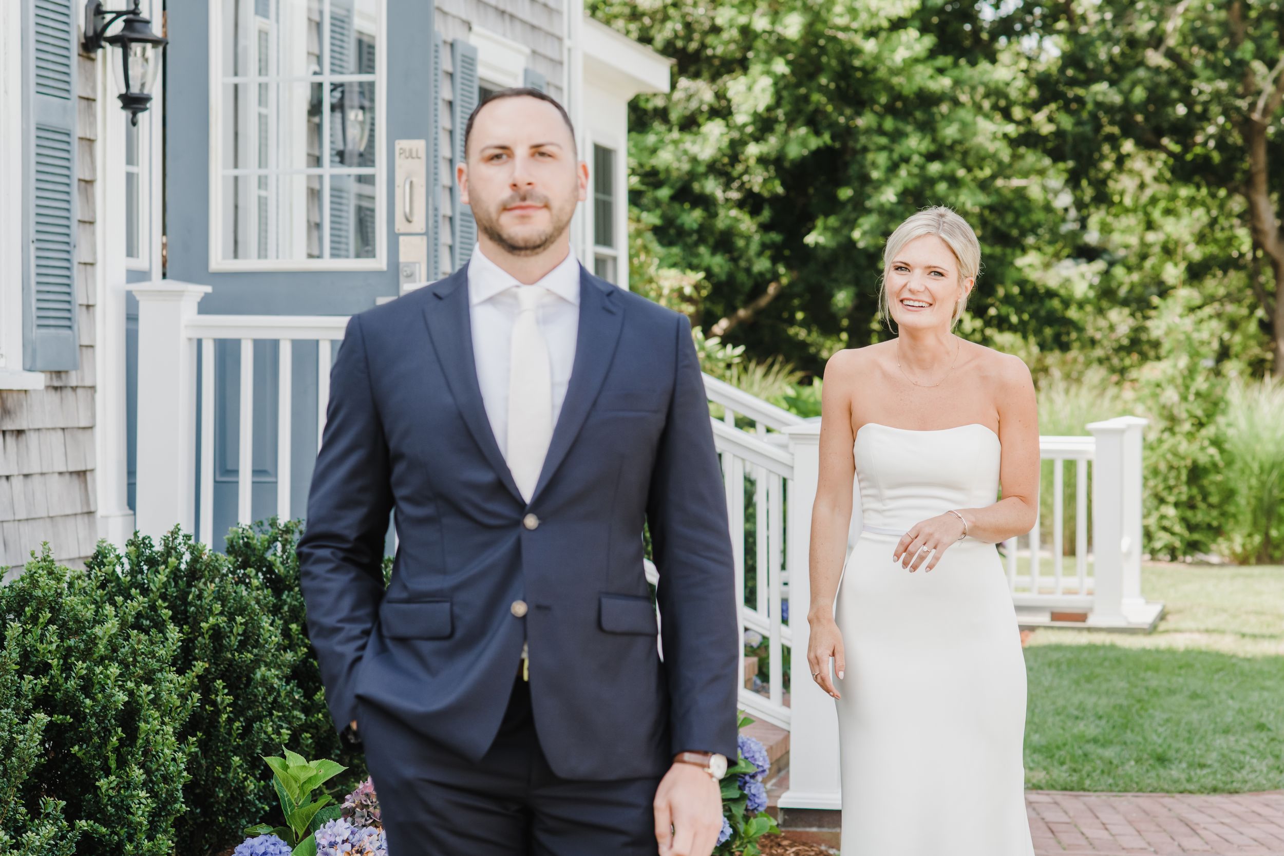 A bride and groom share a sweet first look moment on a white porch with greenery in the background.