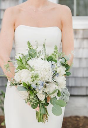 A delicate white bridal bouquet with roses, eucalyptus leaves, and baby's breath against a strapless white wedding dress.