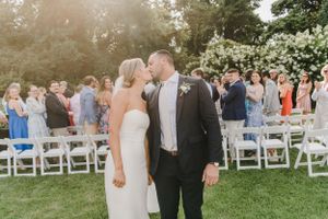 A couple shares a romantic moment at their outdoor garden wedding ceremony with guests and white chairs in the background.
