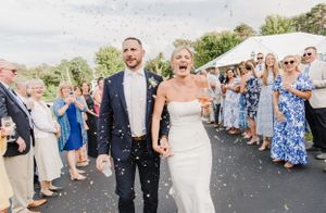 Happy newlyweds exit their wedding ceremony under a shower of confetti while guests cheer and celebrate.