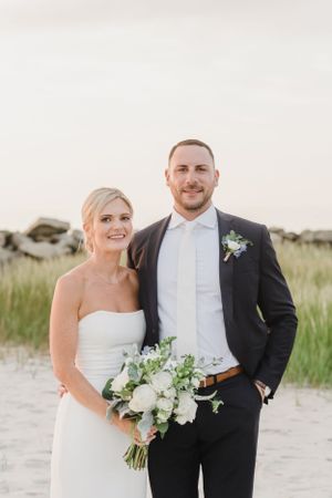 A couple poses at sunset on a beach with sand dunes and sea grass in the background.