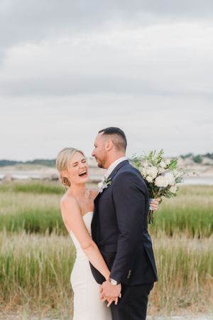 A happy couple shares a joyful moment together in a coastal marsh setting, with a white floral bouquet.