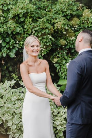 A couple shares a tender moment during their wedding ceremony in a lush garden setting.