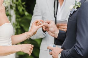 Close-up view of hands exchanging wedding rings during an outdoor ceremony.