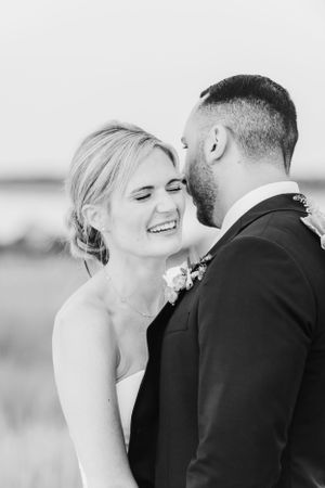 Black and white wedding photo of a laughing bride and groom sharing an intimate moment outdoors.
