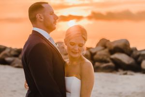 A newlywed couple shares an intimate moment on a rocky beach during a golden sunset.