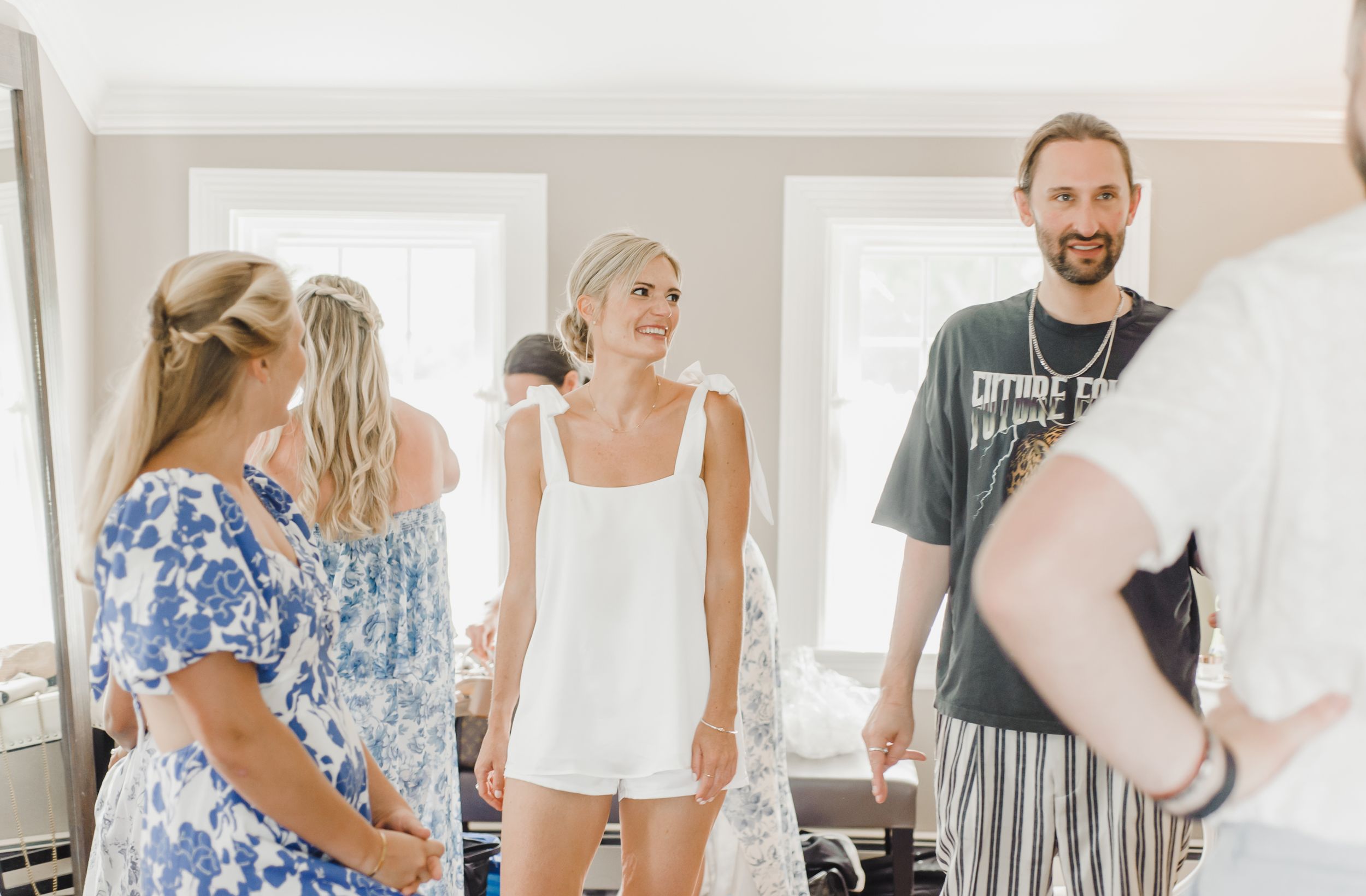 A bright interior room scene shows people gathered together in casual summer attire with natural lighting.