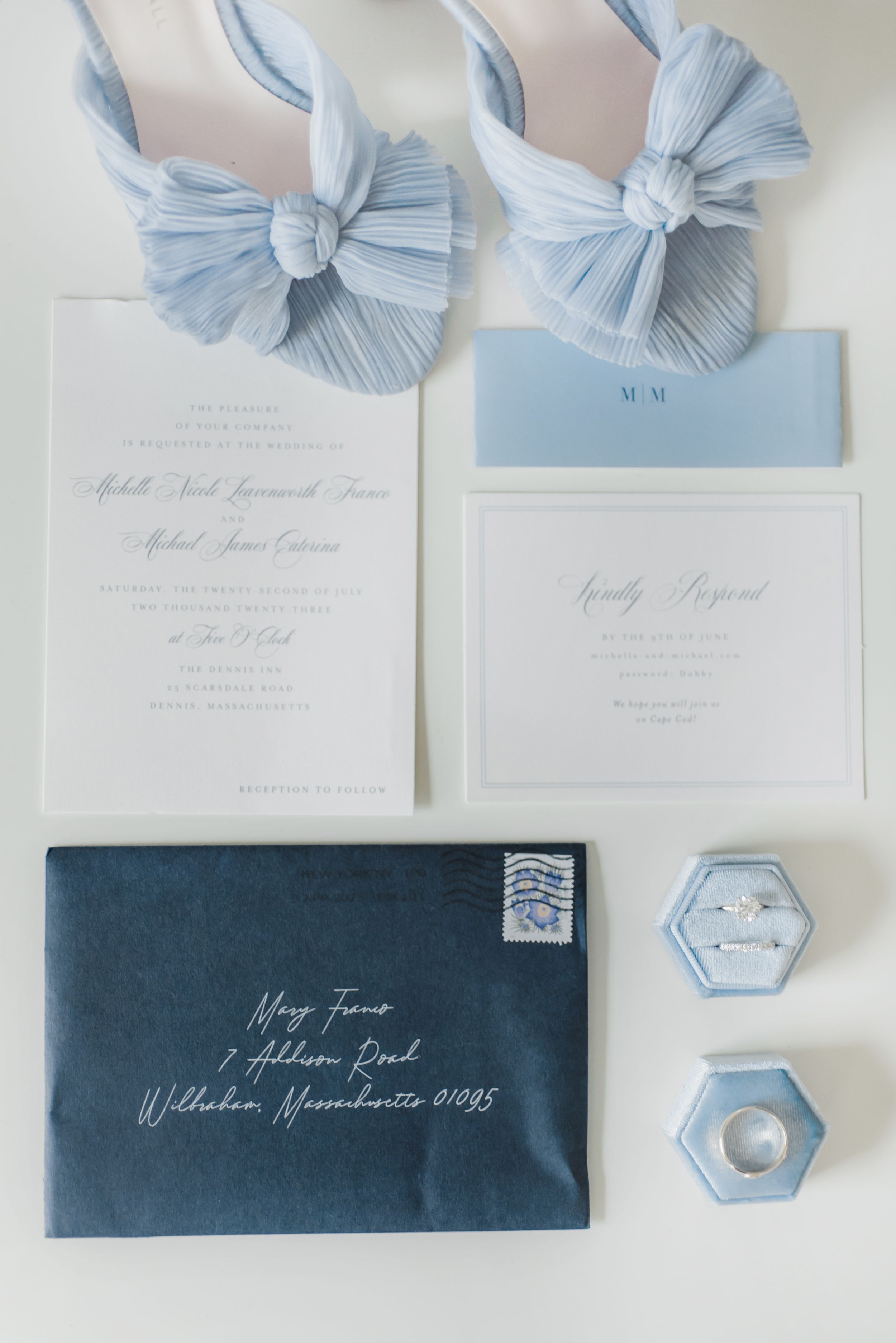Elegant wedding stationery set featuring light blue silk bows, white invitations, and a navy envelope with hexagonal details.
