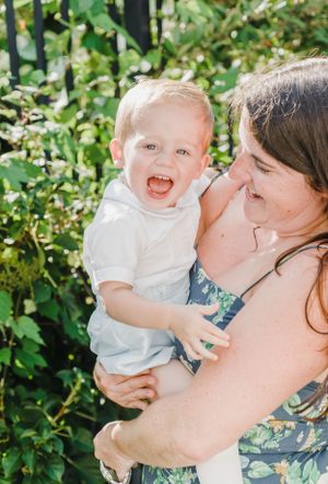 A parent and child share a joyful moment together outdoors against green foliage on a sunny day.