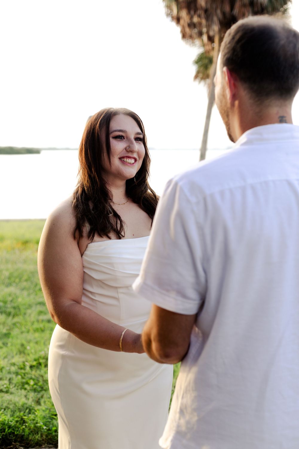 A couple shares a tender moment during their outdoor beach wedding ceremony as palm trees sway in the background.