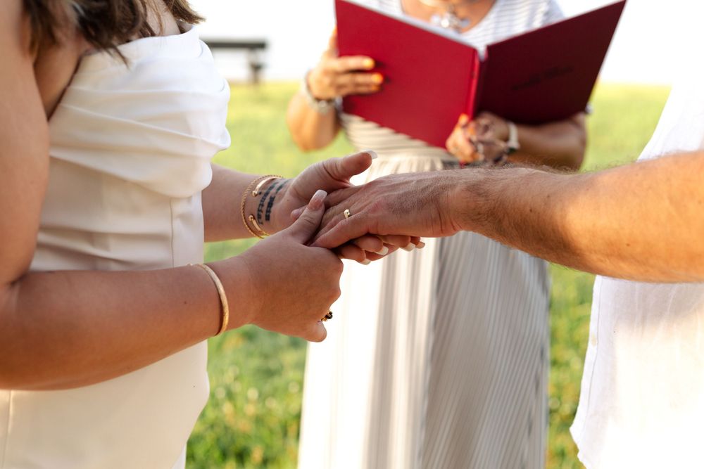 Close-up view of hands exchanging rings during an outdoor wedding ceremony with a red book in the background.