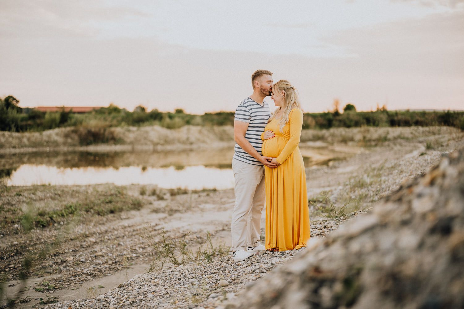 A couple embracing in a desert landscape, wearing yellow and striped outfits during sunset.
