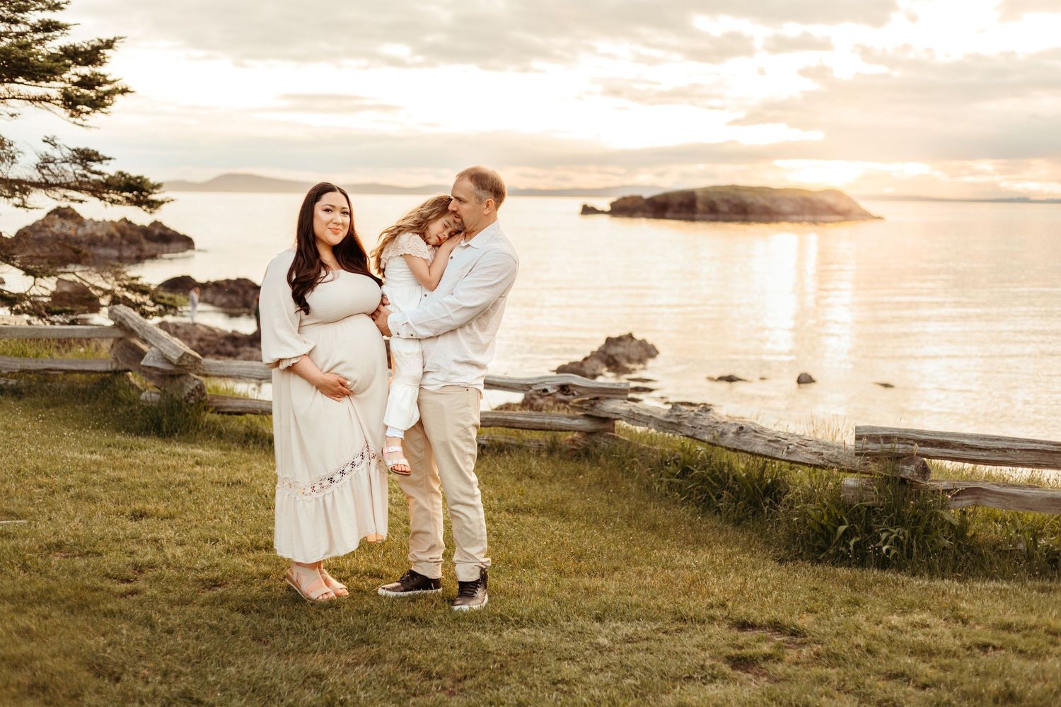 Couple shares intimate moment during sunset maternity photo session by rocky coastline.