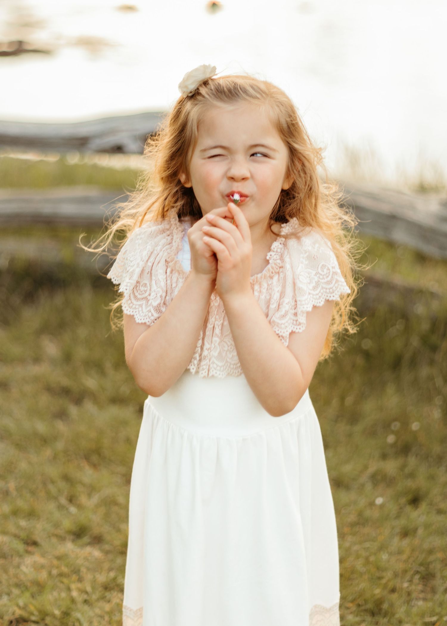 Young girl in white lace dress makes playful expression outdoors.