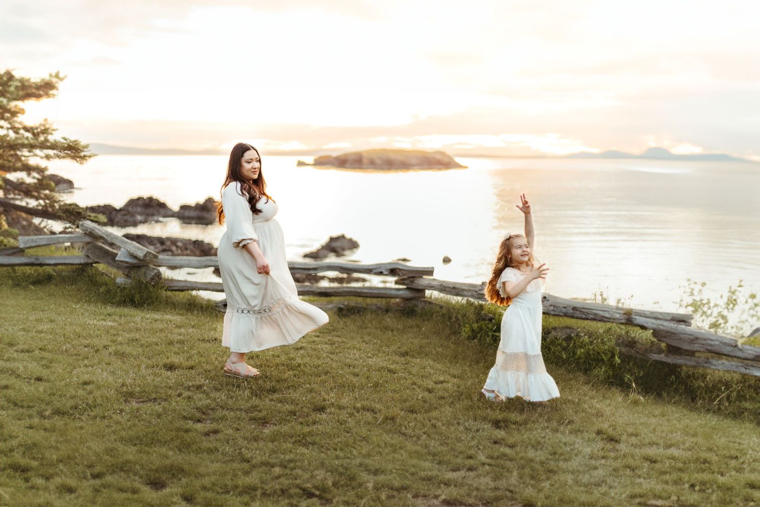Mother and daughter in white dresses jumping joyfully by coastal sunset.